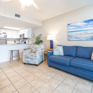 Living space featuring a blue couch with queen sleeper, stylish armchairs, and a vibrant beach-themed painting