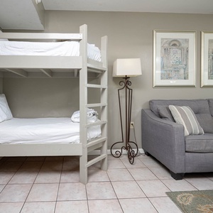 The living area features a twin bunk bed with white linens and a gray sofa adorned with striped pillows beside decorative art
