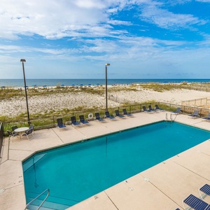 This inviting pool area features a sparkling blue pool, lounge chairs, and a view of the beach just beyond the dunes