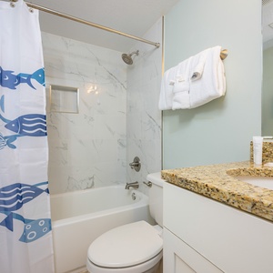 Bright bathroom featuring a granite countertop, a relaxing tub/shower combo, and a stylish blue shower curtain