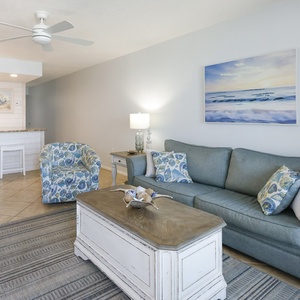 This living area features a comfortable gray sofa, colorful accent chair, and a view of the beach, perfect for relaxation