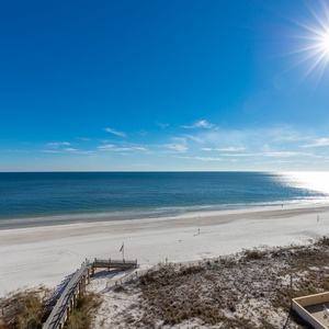 A wide view showcases the tranquil beach front with white sand and gentle waves under a clear blue sky