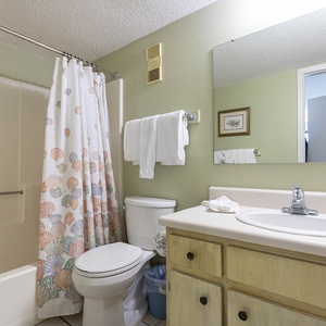 This bathroom features a light green color scheme, a shower with a seashell-patterned curtain, and ample counter space