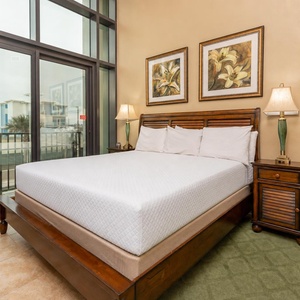 This cozy bedroom features a plush king bed, elegant artwork, and large windows offering a bright view of the surroundings