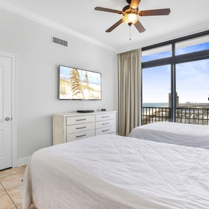 This bedroom features two full beds, a wall-mounted TV, and a stunning beachfront view from the large windows