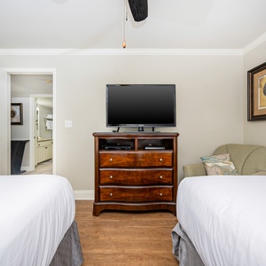 This guest bedroom features two double beds, a wooden dresser with a TV, and a cozy chair, creating a welcoming atmosphere
