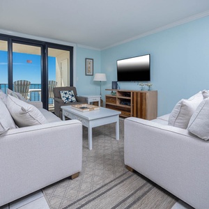 Living area with plush seating and a TV, featuring breathtaking views from the balcony through large glass doors