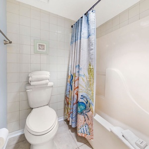 The master bathroom features a tub/shower combo with a colorful shower curtain and neatly stacked towels