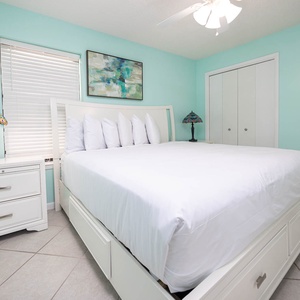 This serene guest bedroom features a king bed with plush pillows, a colorful lamp, and soft aqua walls