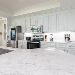 This modern kitchen features stainless appliances, a sleek marble countertop, and light modern cabinetry