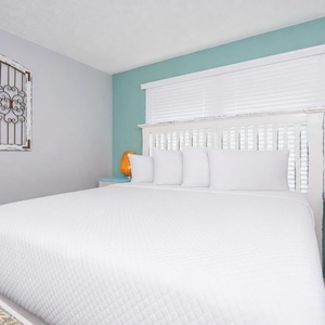 Bright and inviting bedroom featuring a white queen bed, decorative wall art, and a warm orange lamp for cozy ambiance