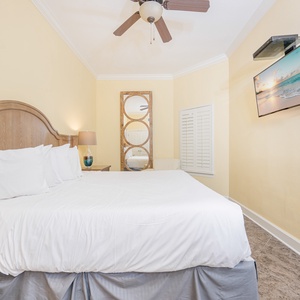 Guest bedroom featuring a plush king bed, soft yellow walls, and a wall-mounted TV for entertainment