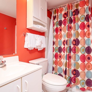 The master bathroom features a vibrant red wall, colorful circular shower curtain, and ample storage for a refreshing stay