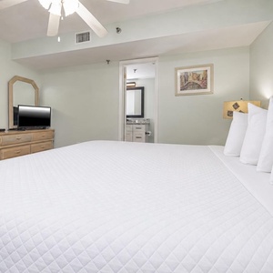 This bedroom features a king bed with white linens, a TV on a dresser, and an en-suite bathroom entrance