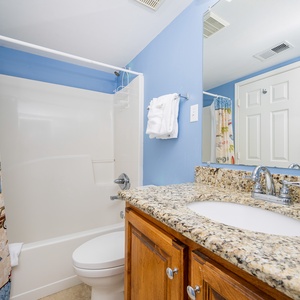 The guest bathroom features a colorful shower curtain, granite countertops, and a bright blue wall, creating a cheerful atmosphere