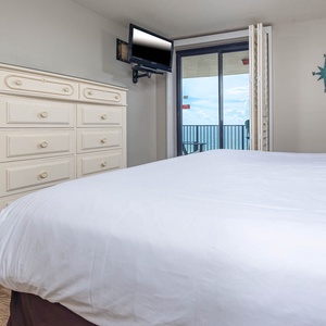 Relax in the comfortable master bedroom featuring a plush king bed and a TV while listening to the sounds of the coast