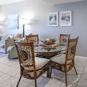 The living area features a cozy sofa with queen sleeper, stylish rattan dining set, and beautiful coastal artwork