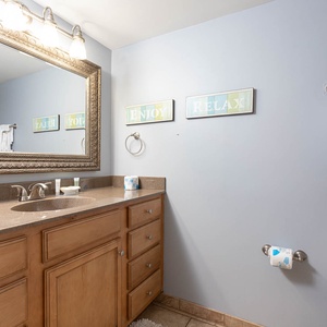 The guest bathroom features a spacious vanity with a large mirror, decorative signs, and a tub/shower combo