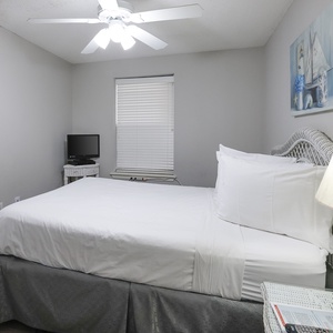 Guest bedroom features a queen bed, a small TV on a stand, and soft lighting from a ceiling fan and bedside lamp
