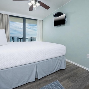 This bedroom features a plush white bed, a mounted TV, and a stunning beachfront view through large sliding glass doors