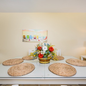 This dining area features a glass table adorned with woven placemats and a vibrant floral centerpiece, perfect for gatherings
