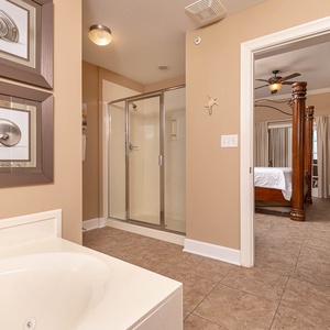 The master bath features a relaxing jetted tub, a walk-in glass shower, and leads to an elegantly decorated bedroom