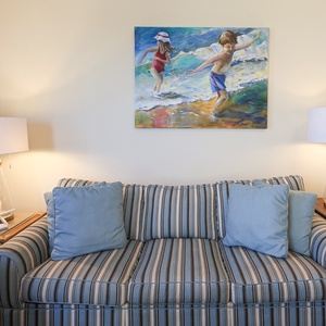Striped sofa with queen sleeper and blue cushions, complemented by a beach painting and a stylish lamp in the living area