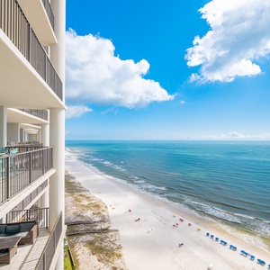 Panoramic views from the balcony showcase the pristine beach and vibrant umbrellas against a clear blue sky