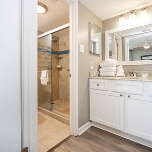The master bathroom features a walk-in shower, a stylish vanity with a granite countertop, and neatly stacked white towels