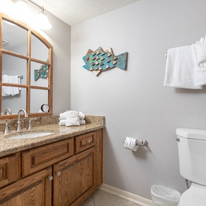 The guest bathroom features a granite countertop with a large mirror, decorative fish art, and neatly arranged white towels