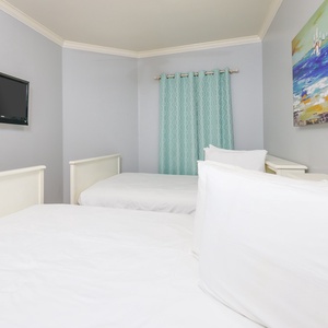 This guest bedroom features two beds, a wall-mounted TV, and cheerful blue accents for a relaxing stay