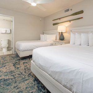 Calming guest bedroom featuring two double beds, a stylish lamp, and a cozy area rug, creating a welcoming atmosphere