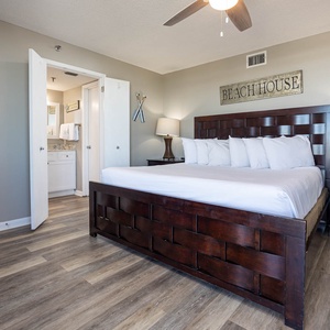 The inviting master bedroom features a king-size bed with white linens, a stylish nightstand, and a view into the bathroom