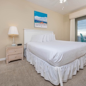 Master bedroom featuring a king bed, bedside lamp, and access to a balcony with turquoise seating overlooking the beach