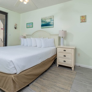 Unwind in the master bedroom featuring a large king bed, soft decor, and access to a balcony with inviting beach views