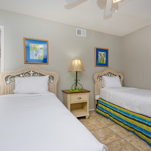 This guest bedroom features two twin beds with colorful bedding, bright artwork, and a cozy lamp for a relaxing stay