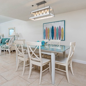 This inviting living area features a turquoise sofa with queen sleeper, a glass dining table, and vibrant surfboard art