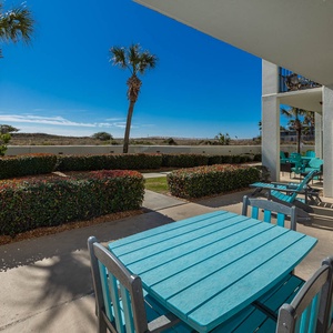 Turquoise patio set surrounded by lush greenery and palm trees under a clear blue sky