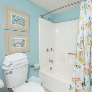 The guest bath features a cheerful aqua wall, a tub/shower combo, and vibrant shower curtains for a refreshing touch