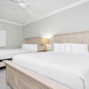 Rest in this serene guest bedroom featuring two queen beds, soft linens, and a stylish lamp for a cozy retreat