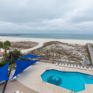 Take in the serene beach view while relaxing by the inviting pool area adorned with vibrant blue canopies