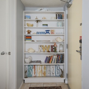 This welcoming entryway features a decorative shelf filled with beach-themed decor and books, setting a relaxed vacation vibe