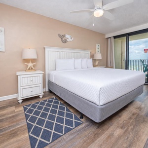 The master bedroom features a cozy king bed, beach-themed decor, and a balcony with a beautiful view of the coastline