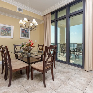 Dining area with a glass table, elegant decor, and large windows showcasing a beautiful coastal view