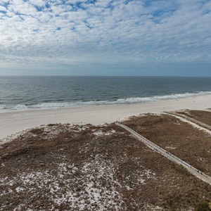 Expansive view of the beach with white sand and gentle waves, framed by lush greenery and a winding boardwalk