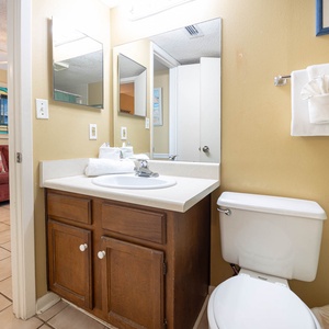 This bathroom features a clean design with a single sink vanity, ample mirrors, and a cozy view of the adjoining living area