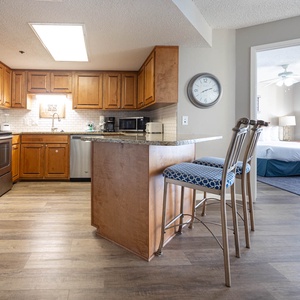 The fully-equipped kitchen features wooden cabinetry, a breakfast bar with stylish stools, and a glimpse of the cozy bedroom