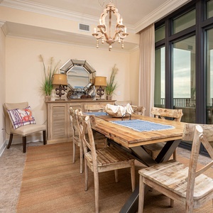 This dining area features a rustic wooden table, elegant chandelier, and stunning beach front views through large windows