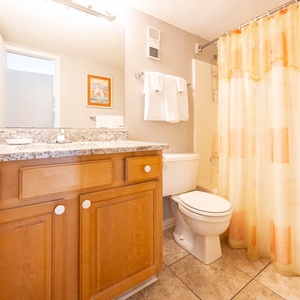 This bathroom features a granite countertop, bright yellow shower curtain, and a spacious mirror for your convenience