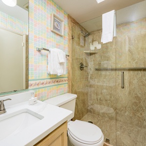 The bathroom features a glass shower, marble accents, and a cheerful pastel tile design, offering a refreshing experience